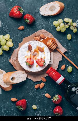 Camembert Käse mit Trauben, Mandelnüssen, Baguette, Erdbeeren, Honig, Wein vor rustikalem, dunklem Hintergrund. Draufsicht. Speicherplatz kopieren. Gourmet-Vorspeise für Stockfoto