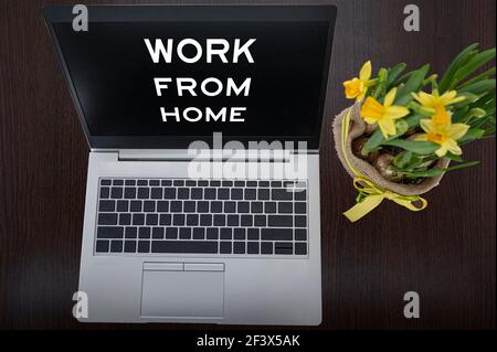Draufsicht auf silbernen Laptop mit Beschriftung Arbeit von zu Hause und Pflanze auf Tisch. Stockfoto