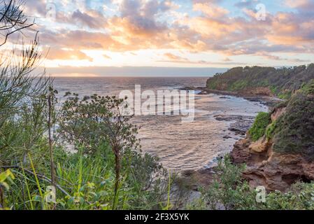 Der warme Sommersonnenaufgang spiegelt sich in den niedrigen Cumulus-Wolken und erleuchtet die zerklüftete Küste am Bendalong Point, New South Wales, Australien Stockfoto