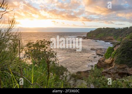 Der warme Sommersonnenaufgang spiegelt sich in den niedrigen Cumulus-Wolken und erleuchtet die zerklüftete Küste am Bendalong Point, New South Wales, Australien Stockfoto