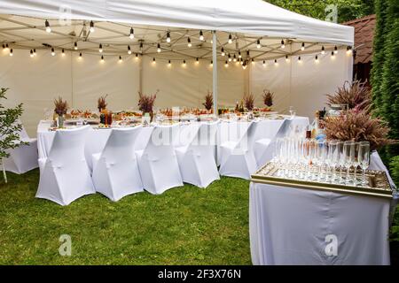 Weißes Hochzeitszelt mit weißen Stühlen. Bankettsaal unter einem Zelt für eine Hochzeit oder ein anderes Abendessen mit Catering. Stockfoto