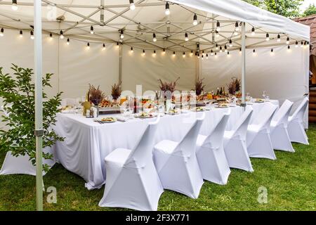 Weißes Hochzeitszelt mit weißen Stühlen. Bankettsaal unter einem Zelt für eine Hochzeit oder ein anderes Abendessen mit Catering. Stockfoto