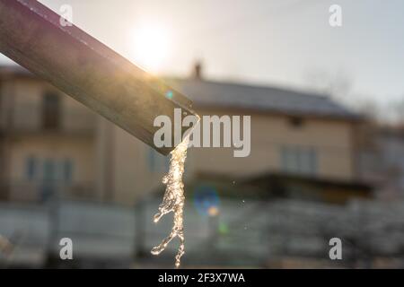 Schmelzende Eiszapfen, auf der Pipeline im frühen Frühjahr. Auf einem unscharfen Sonnengrund. Stockfoto