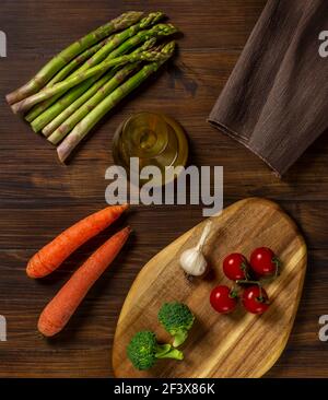 Zusammensetzung von verschiedenen Gemüse mit Spargel, Kirschtomaten, Karotten, Knoblauch, Brokkoli und cruet mit Olivenöl, auf Holztisch und Holzschnitt Stockfoto