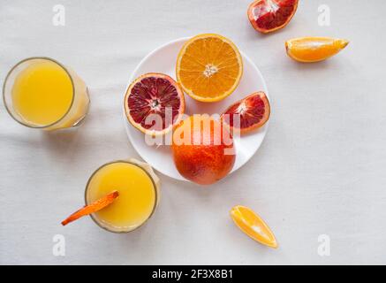 Flach legen von frischen süßen und saftigen Blutorangen und Orangen, ganz und auf einem weißen Teller geschnitten. Frischer Orangensaft mit in Scheiben geschnittenen Orangen. Stockfoto
