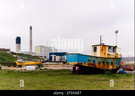 Foto des kleinen Fischerhafens Boddam mit einem rostigen alten Fischerboot im Vordergrund und dem Kraftwerk Peterhead im Hintergrund. Stockfoto