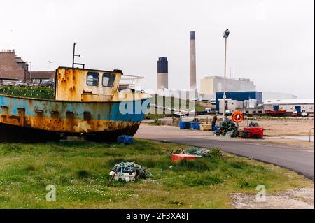 Foto des kleinen Fischerhafens Boddam mit einem rostigen alten Fischerboot im Vordergrund und dem Kraftwerk Peterhead im Hintergrund. Stockfoto