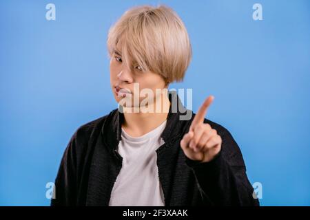 Porträt eines ernsthaften koreanischen Mann zeigt ablehnende Geste durch Stop-Finger-Zeichen. Asian Kerl mit gefärbten blonden Haaren isoliert auf blauem Hintergrund. Stockfoto