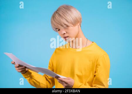 Junger asiatischer Mann prüft Dokumente, Stromrechnungen, Bericht. Kerl isoliert auf gelbem Hintergrund. Stockfoto