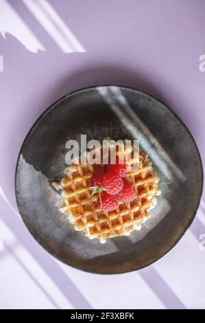 Hausgemachte Wiener Waffeln mit reifen Himbeeren auf einem rosa Hintergrund mit einem schönen abstrakten Licht. Draufsicht. Kopierbereich. Stockfoto