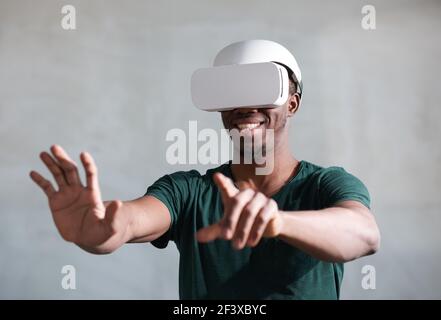 Junger afrikanischer Mann, der Konsolenspiele trägt, das vr-Headset isoliert Auf grauem Hintergrund Stockfoto