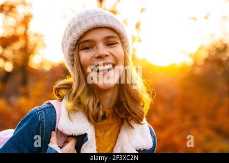 Lächelndes Mädchen in gestricktem Hut zu Fuß im Herbst Park, Rucksack tragen Stockfoto