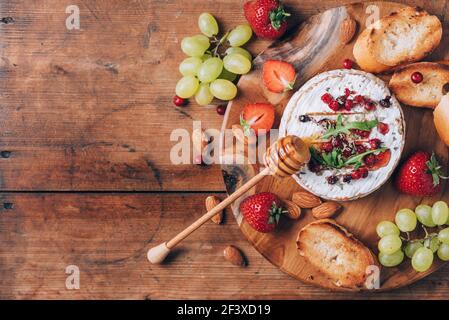 Gebackener Camembert-Käse mit Honig, Rucola, Preiselbeere, geröstetem Brot, Traube, Erdbeeren, Mandelnüsse auf Holzbrett. Draufsicht. Speicherplatz kopieren. Romantisch Stockfoto