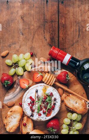 Romantische Dattsnacht. Valentinstag, Liebeskonzept. Gebackener Camembert-Käse mit Honig, Rucola, Cranberry, Wein, geröstetem Brot, Traube, Erdbeeren Stockfoto
