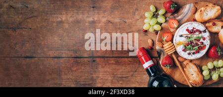 Romantische Dattsnacht. Valentinstag, Liebeskonzept. Gebackener Camembert-Käse mit Honig, Rucola, Cranberry, Wein, geröstetem Brot, Traube, Erdbeeren Stockfoto