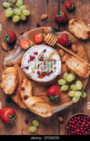Gebackener Camembert-Käse mit Honig, Rucola, Preiselbeere, geröstetem Brot, Traube, Erdbeeren, Mandelnüsse auf Holzbrett. Draufsicht. Speicherplatz kopieren. Romantisch Stockfoto
