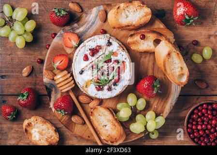 Gebackener Camembert-Käse mit Honig, Rucola, Preiselbeere, geröstetem Brot, Traube, Erdbeeren, Mandelnüsse auf Holzbrett. Draufsicht. Speicherplatz kopieren. Romantisch Stockfoto