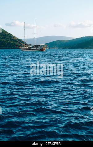 Die Yacht gleitet auf blauem Wasser vor der Kulisse der Berge vor der Küste der Stadt Perast. Stockfoto