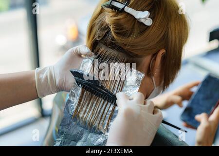 Attraktive Brünette gründlich färben Haare der weiblichen Klienten, während sie im Stuhl sitzt im Beauty Salon Friseur Stockfoto