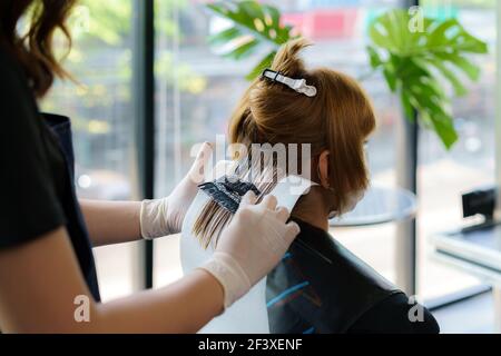 Attraktive Brünette gründlich färben Haare der weiblichen Klienten, während sie im Stuhl sitzt im Beauty Salon Friseur Stockfoto