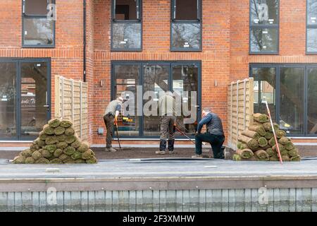 Männer Vorbereitung Boden Rasen oder Rasen vor neuen Häusern, Großbritannien, mit Haufen von Rasen Rollen zu legen Stockfoto