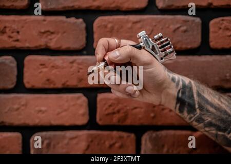 Nahaufnahme von Hand altmodischen Hipster Tattoo Künstler hält Tattoo Maschine auf einem Backstein Hintergrund. Stockfoto