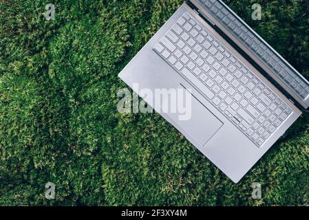 Laptop auf grünem Gras, Moos Hintergrund. Ökologie Reisen, Arbeit außerhalb Büro Konzept. Achtsamkeit, biophiles Design, Konzept ausstecken. Digitale Entgiftung Stockfoto