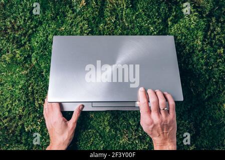 Achtsamkeit, biophiles Design, Konzept ausstecken. Hände auf Computer, Laptop-Tastatur über grünem Gras, Moos Wald Hintergrund. Draufsicht. Digitale Entgiftung Stockfoto