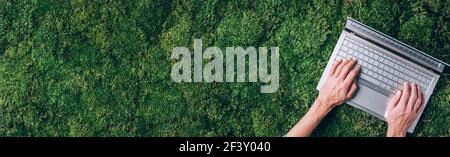 Hände auf Computer, Laptop-Tastatur über grünem Gras, Moos Wald Hintergrund. Draufsicht. Achtsamkeit, biophiles Design, Konzept ausstecken. Digitale Entgiftung Stockfoto
