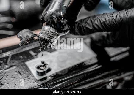 Nahaufnahme Foto von Tattoo Master in schwarzen Handschuhen Gießen Tinten in Kunststoff-Tasse. Stockfoto