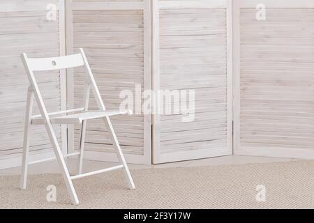 Ein einfacher weißer Stuhl vor dem Hintergrund einer hölzernen Leinwand. Pastellfarben. Minimalistisches Design. Stockfoto