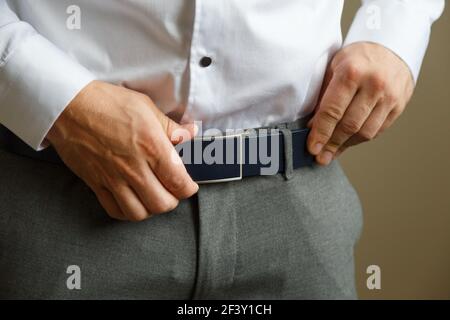 Ein Mann in blauer Hose und einem weißen Hemd knöpfte einen braunen Ledergürtel. Er hat eine Uhr an der Hand. Stockfoto