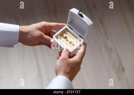 Weiße Holzkiste mit zwei goldenen Eheringen in den Händen des Bräutigams, Nahaufnahme, Hochzeitsaccessoires Stockfoto