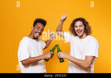 Porträt einer zwei fröhlichen jungen Männer beste Freunde, die mit Bierflaschen über gelbem Hintergrund getoasten Stockfoto
