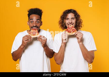 Portrait von zwei hungrigen jungen Männern, die isoliert Pizza essen Auf gelbem Hintergrund Stockfoto