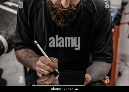 Nahaufnahme junger Mann Tattoo-Künstler mit Bart Zeichnung Bleistift und Skizze stehen in Werkstatt Ort. Stockfoto