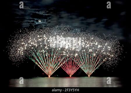 Schillerndes Feuerwerk bei einem Sommerfeuerwerk Wettbewerb - die Vollmond scheint durch die Wolken Stockfoto