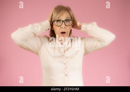 Überrascht glücklich Senior Frau in eleganten Hemd isoliert über rosa Hintergrund. Stockfoto
