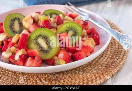 Gesunder Obstsalat mit Erdbeeren, Bananen und Kiwis auf einem Teller mit Gabel Stockfoto