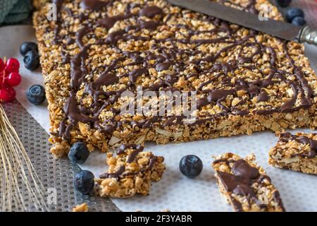 Frisch gebackene hausgemachte Müsliriegel mit Nüssen, gepufftem Hafer und Amaranth, Honig und Ahornsirup. Garniert mit dunkler Schokolade auf einem Tablett Stockfoto