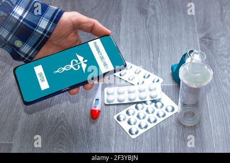 Eine Männerhand mit einer pharmazeutischen App mit verschiedenen Medikamenten im Hintergrund. Konzept der Kauf von Medikamenten durch mobile Anwendung Stockfoto
