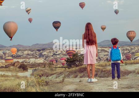 Zwei Kinder Mädchen in einem rosa Kleid und ein Junge Mit Rucksack-Look auf bunten Ballons in den Himmel darüber Die sandigen Berge Stockfoto