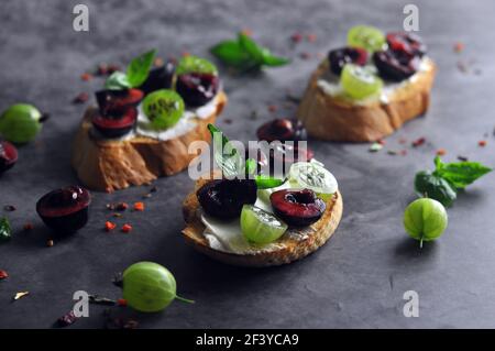 Bruschetta mit Frischkäse, Kirsche und Stachelbeere Close-Up auf dunklem Hintergrund Stockfoto
