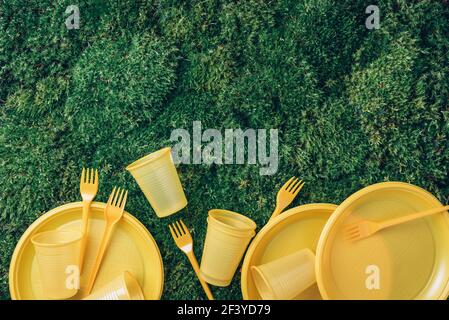 Umweltverschmutzung. Einweggeschirr aus Kunststoff - Plastikteller, Gabeln, Löffel, Messer. Gelbes Plastikgeschirr auf grünem Gras, Moos Stockfoto