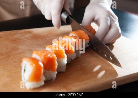 Nahaufnahme des Prozesses der Zubereitung von rollendem Sushi. Zubereitung des Sushi mit Sauce und Sesam, gießt köstliche frische Brötchen mit einer Sauce. Dunkler Rücken Stockfoto