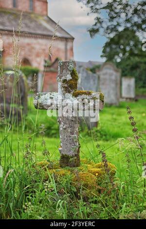 Altes hölzernes Kreuz, das mit Moos auf einem Friedhof bedeckt ist England Stockfoto