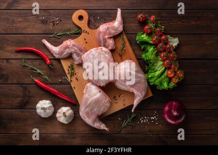 Frisches rotes Kaninchenfleisch mit frischem Gemüse auf einem Holzschneidebrett, Draufsicht Stockfoto