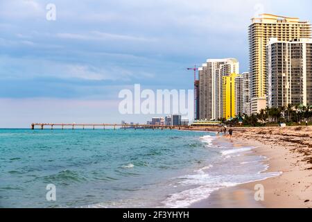 Sunny Isles Beach, USA - 7. Mai 2018: Wolkenkratzer in Apartmenthotels oder Eigentumswohnungen bei Sonnenuntergang in Miami, Florida mit Menschen am Pier und Wellen Stockfoto