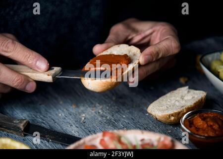 Nahaufnahme eines jungen kaukasischen Mannes, der eine vegane Vorspeise zubereitet, indem er eine vegane Version der spanischen Sobrasada mit sonnengetrockneten Tomaten und al verteilt Stockfoto