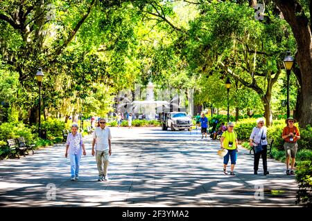 Savannah, USA - 11. Mai 2018: Berühmter Wasserbrunnen im Forsyth Park, Georgia am sonnigen Sommertag mit älteren Menschen Paar zu Fuß auf Gasse Straße Pat Stockfoto